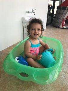 A baby wearing a bathing suit plays in a bathtub.