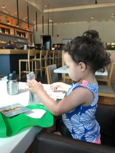 A baby sits at a table reading a menu.