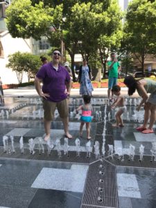 A woman and a toddler play in a water fountain together.