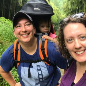 two women hiking, the woman on the left is carrying a baby in a backpack