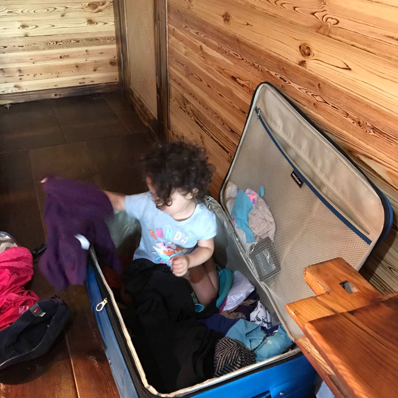 a child sits in a suitcase surrounded by clothes